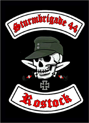 Totenschädel kombiniert mit olivfarbener Feldmütze vor zwei gekreuzten Dolchen, einem eisernen Kreuz sowie roter Beschriftung in gebrochener Schrift mit schwarzer Umrandung auf weißen Bannern „Sturmbrigade 44“ und „Rostock“