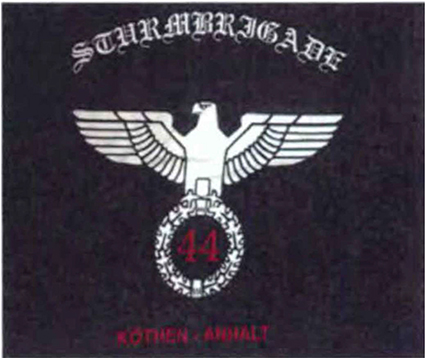 Weißer Schriftzug in gebrochener Schrift „Sturmbrigade“ mit Reichsadler und Siegerkranz sowie der roten Zahl „44“ und dem Ortsnamen Köthen-Anhalt in roter Schrift auf schwarzem Hintergrund