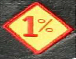 Das gelbe Kennzeichen ist rot umrandet und hat die Form einer Raute. Es zeigt eine rote Eins sowie direkt dahinter ein rotes Prozentzeichen.