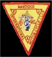 Dieses gelbe Kennzeichen mit roter Umrandung in umgekehrter Dreiecksform zeigt einen nach links blickenden dickbäuchigen Mann mit Sombrero, in dem sich zwei Einschusslöcher befinden. Pistole und Schwert hält er in den Händen. Links des Mannes befindet sich das rautenförmige „1 Prozent Zeichen“, rechts die Abkürzung „MC“ in einem rot umrandetem Viereck. Um den Mann und die beiden Abzeichen herum, befindet sich ein weiteres rotes umgekehrtes Dreieck, in dessen drei Ecken von oben links im Uhrzeigersinn gelesen die Großbuchstaben E A A abgebildet sind. Oberhalb des Mannes und außerhalb des inneren umgekehrten Dreiecks steht in roten Großbuchstaben der Name „BANDIDOS“, rechts, entlang der nach unten zeigenden Seite, die Bezeichnung „MOTORCYCLE CLUB“ und links der Zusatz „INTERNATIONAL“.