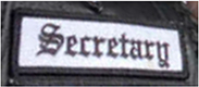 Dieses weiße Kennzeichen mit schwarzer Umrandung in Form eines Rechtecks enthält die Funktionsbeschreibung „Secretary“, übersetzt Schriftführer, in schwarzen Buchstaben.