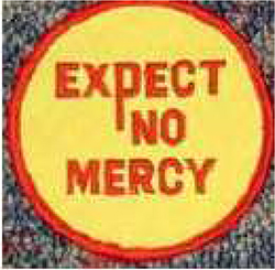 Dieses gelbe Kennzeichen mit roter Umrandung in Form eines Kreises, enthält die Aussage „EXPECT NO MERCY“, übersetzt „Erwarte keine Gnade“ in roten Großbuchstaben.