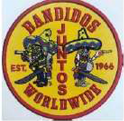 Dieses gelbe Kennzeichen mit roter Umrandung in Form eines Kreises, enthält sowohl einen nach rechts sowie einen nach links blickenden dickbäuchigen Mann mit Sombrero mit Pistole und Schwert in den Händen. Ein nach obenhin gerundeter Schriftzug in roten Großbuchstaben enthält den Namen „BANDIDOS“, mittig zwischen den beiden Männern mit einer roten Buchstabenfolge von oben nach unten steht „JUNTOS“, übersetzt alle. Darunter befindet sich ein nach untenhin gerundeter Schriftzug „WORLDWIDE“, übersetzt weltweit, ebenfalls in roten Großbuchstaben. Jeweils links und rechts der Männer steht in Rot die Jahresangabe „EST. 1966“.